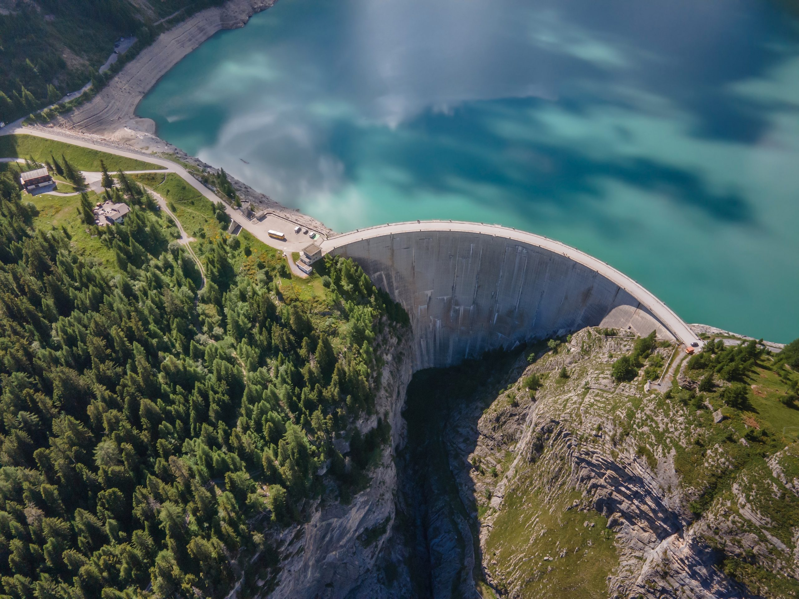 Aerial view of a concrete arch dam holding back a turquoise mountain reservoir